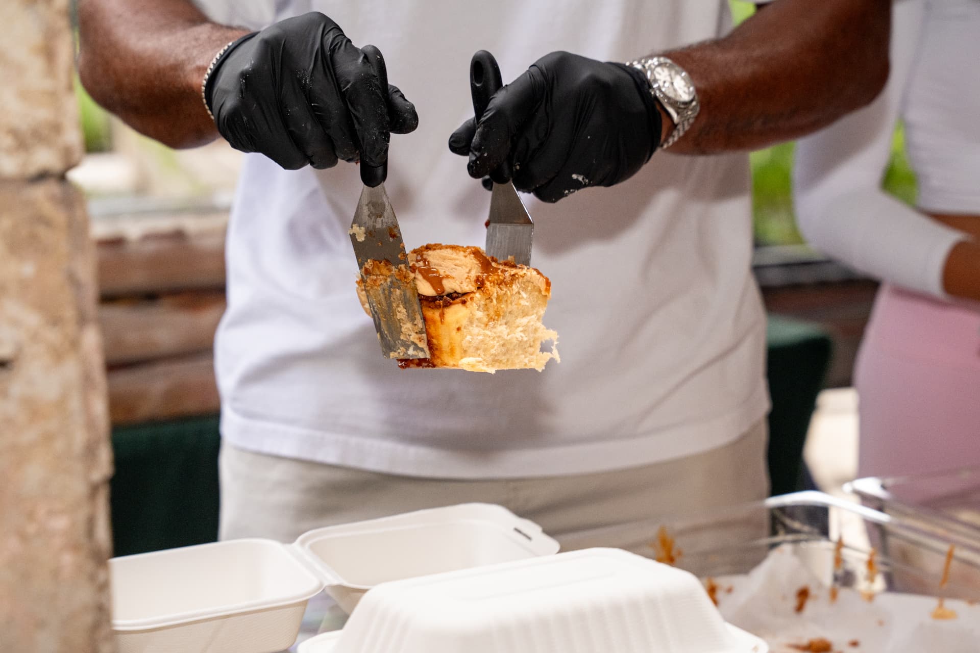 Two hands pulling apart a warm cinnamon roll with stretchy frosting