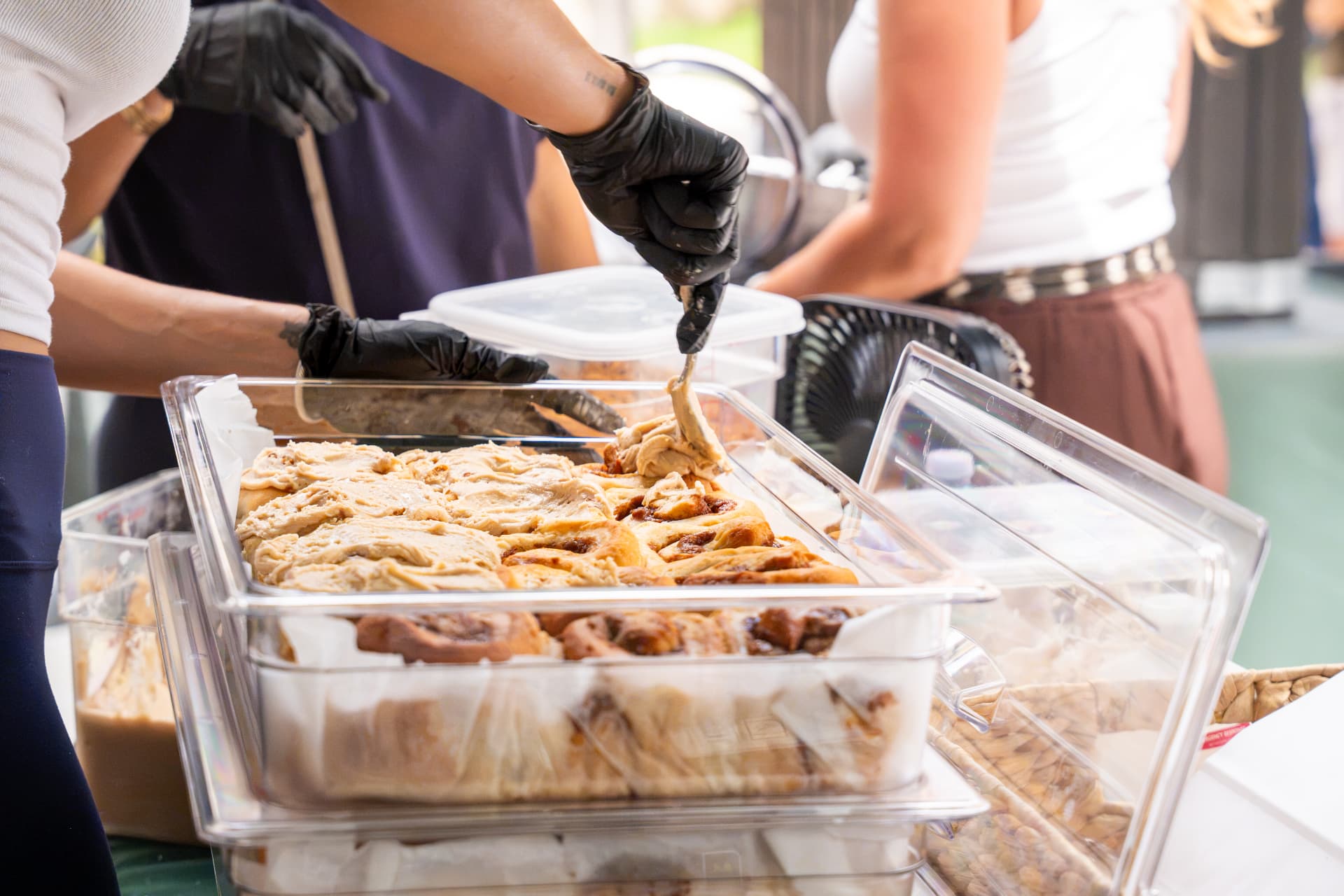 Frosting being spread over a tray of warm cinnamon rolls at the market